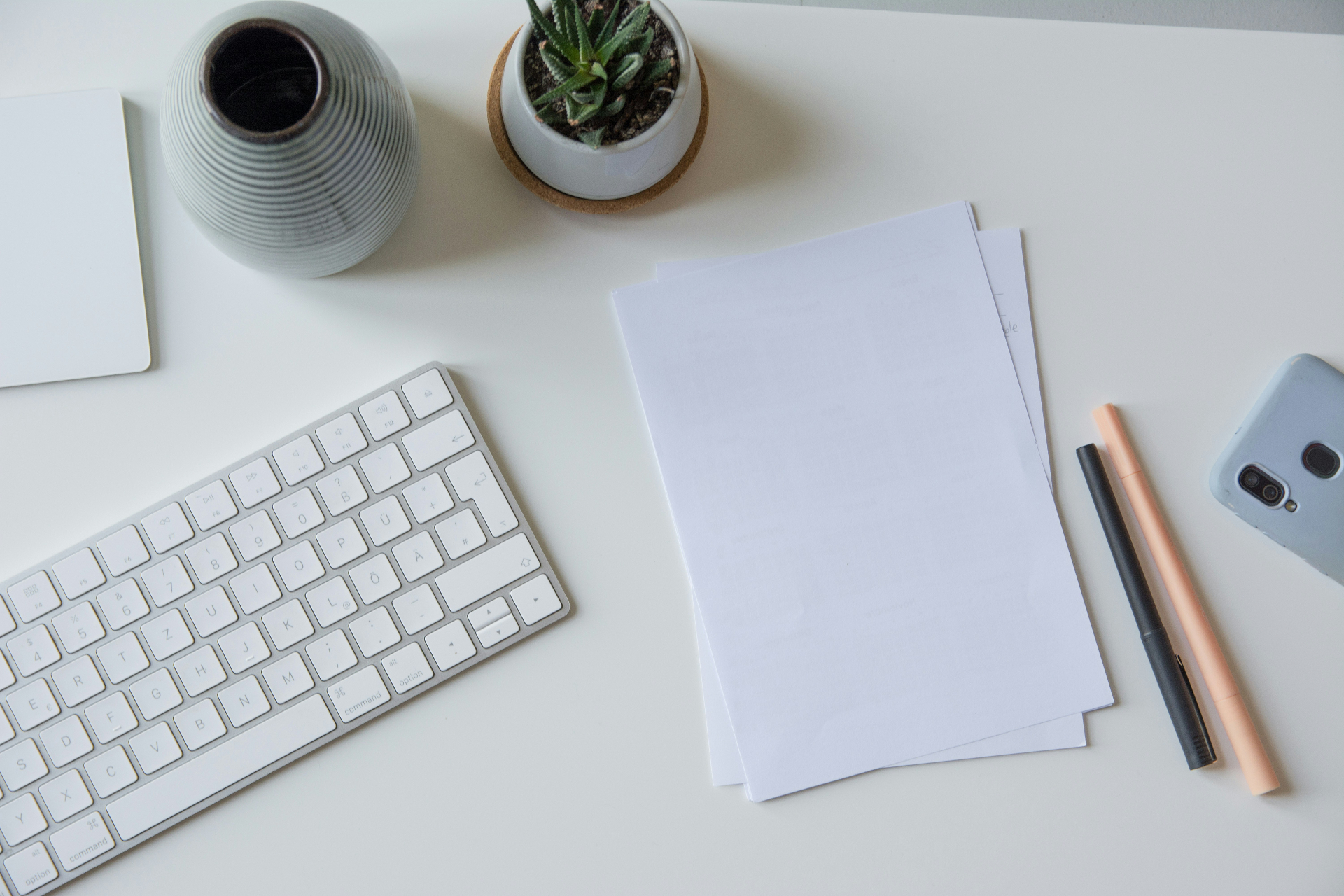Clean light grey desk surface with a plain notebook, pen and blank paper in soft natural light.